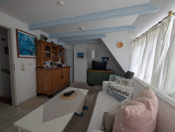 Heller Wohnraum mit Sofa, Couchtisch und Holzschrank, große Fenster mit Gardinen.