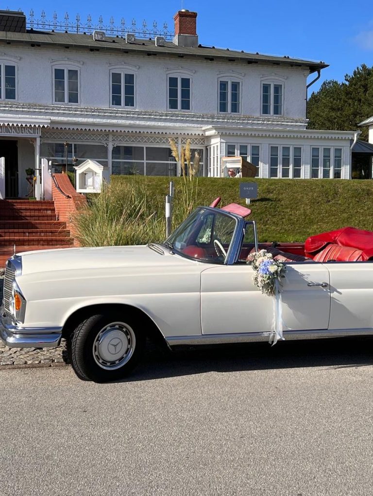 Ein weißes Cabriolet mit rotem Stoff und Blumen, vor einem modernen Gebäude geparkt.